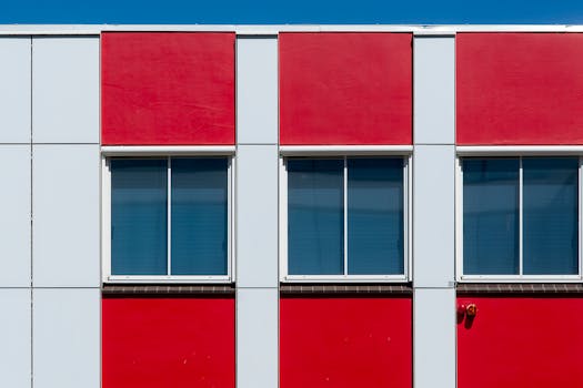 Contemporary building facade with red and white panels featuring windows under a clear blue sky.