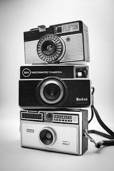 Black and white photo of three stacked vintage Instamatic cameras, showcasing retro design.