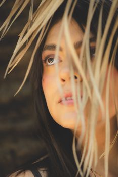 Close-up artistic portrait of a young woman looking thoughtful through palm leaves.