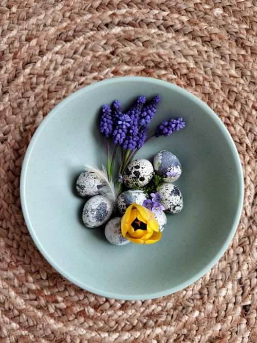 Free Top-down view of quail eggs with purple and yellow flowers in a mint green bowl. Stock Photo