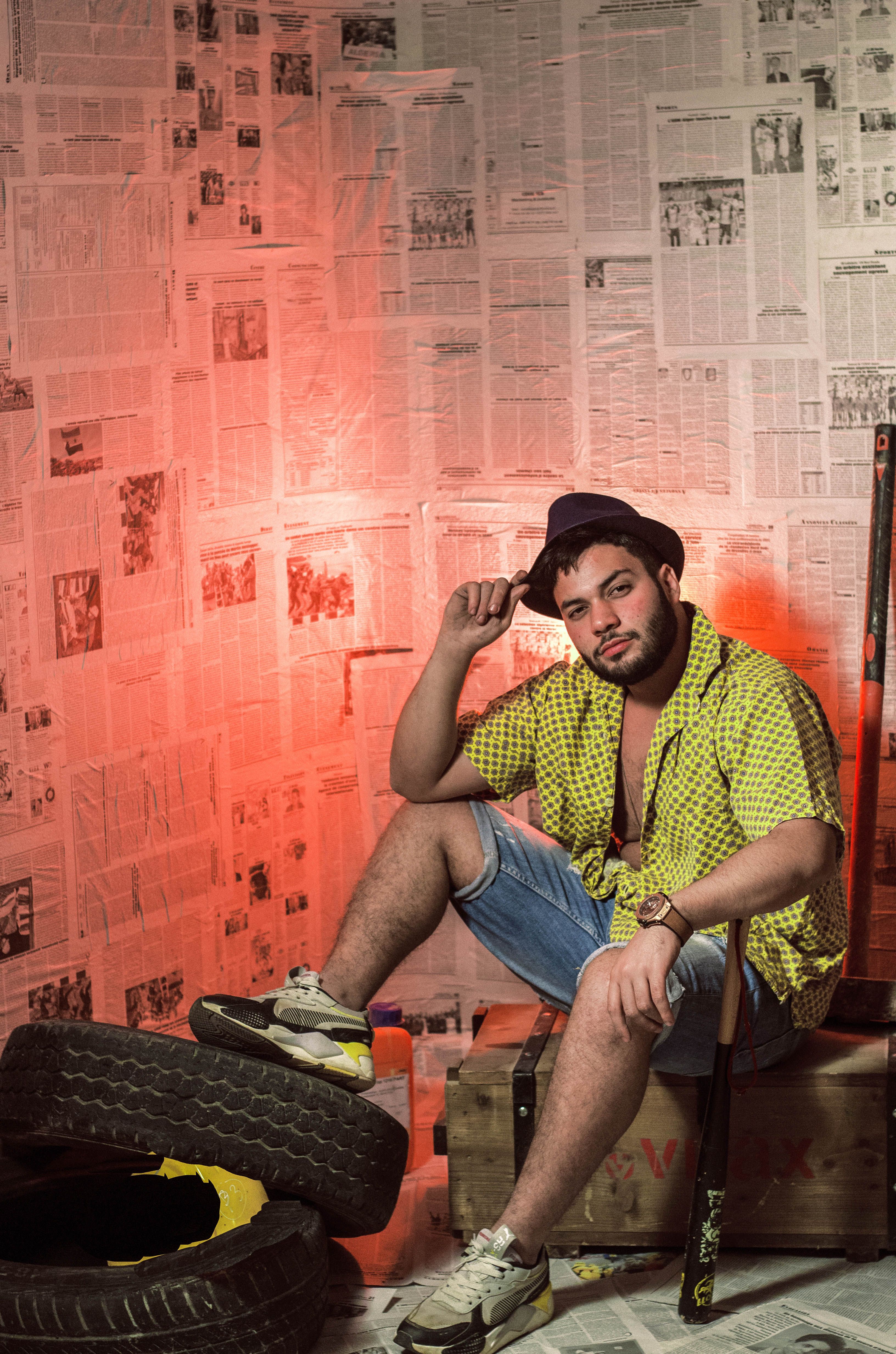 Man seated in an industrial setup with striking fashion against newspaper wall backdrop.