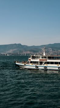 White ferry boat on a clear sea with mountain backdrop, perfect travel scene.