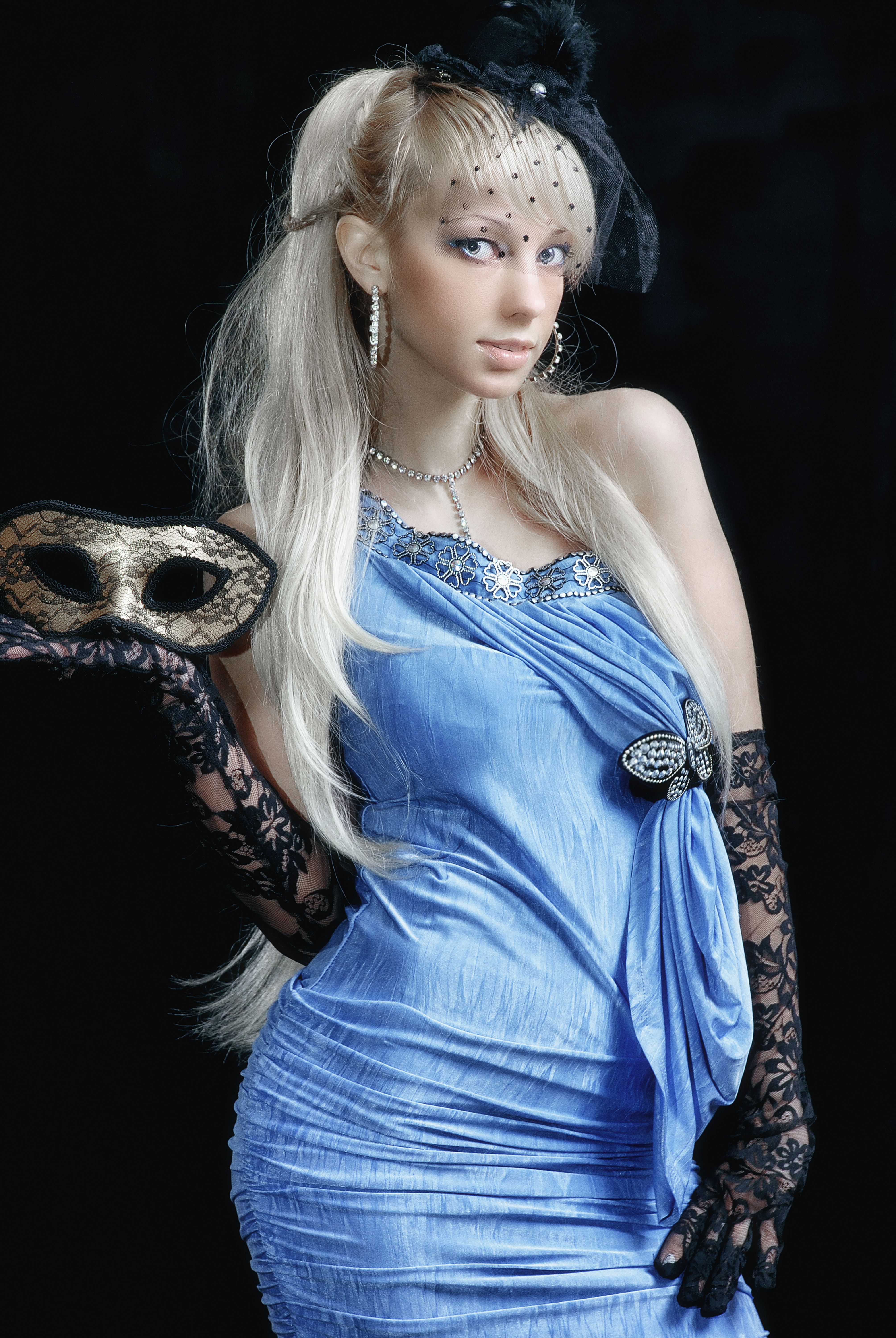 Stylish woman in blue dress and lace gloves holding a Venetian mask, exuding mystery and elegance.