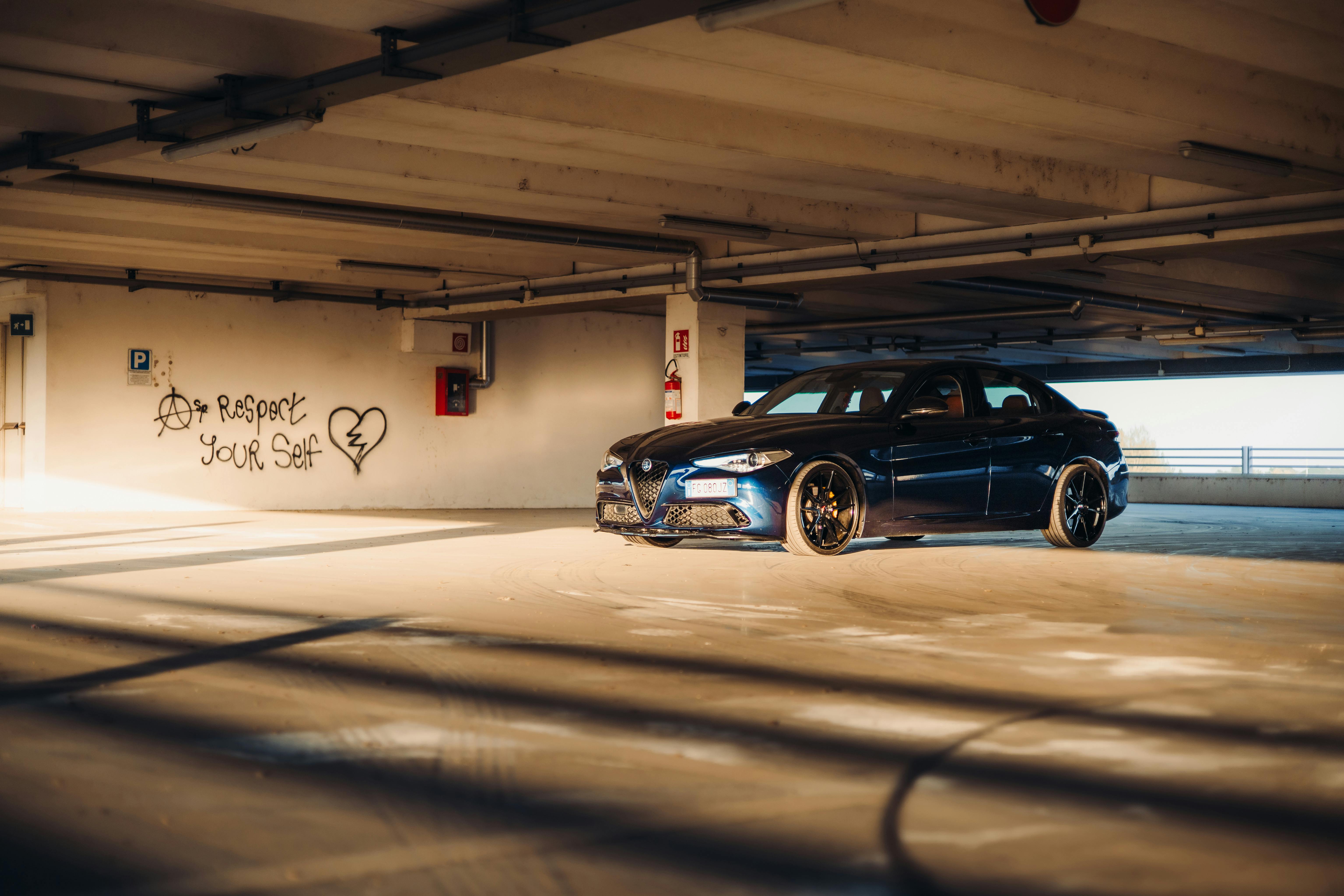 Luxury car parked in sunlit urban garage with graffiti art on walls.
