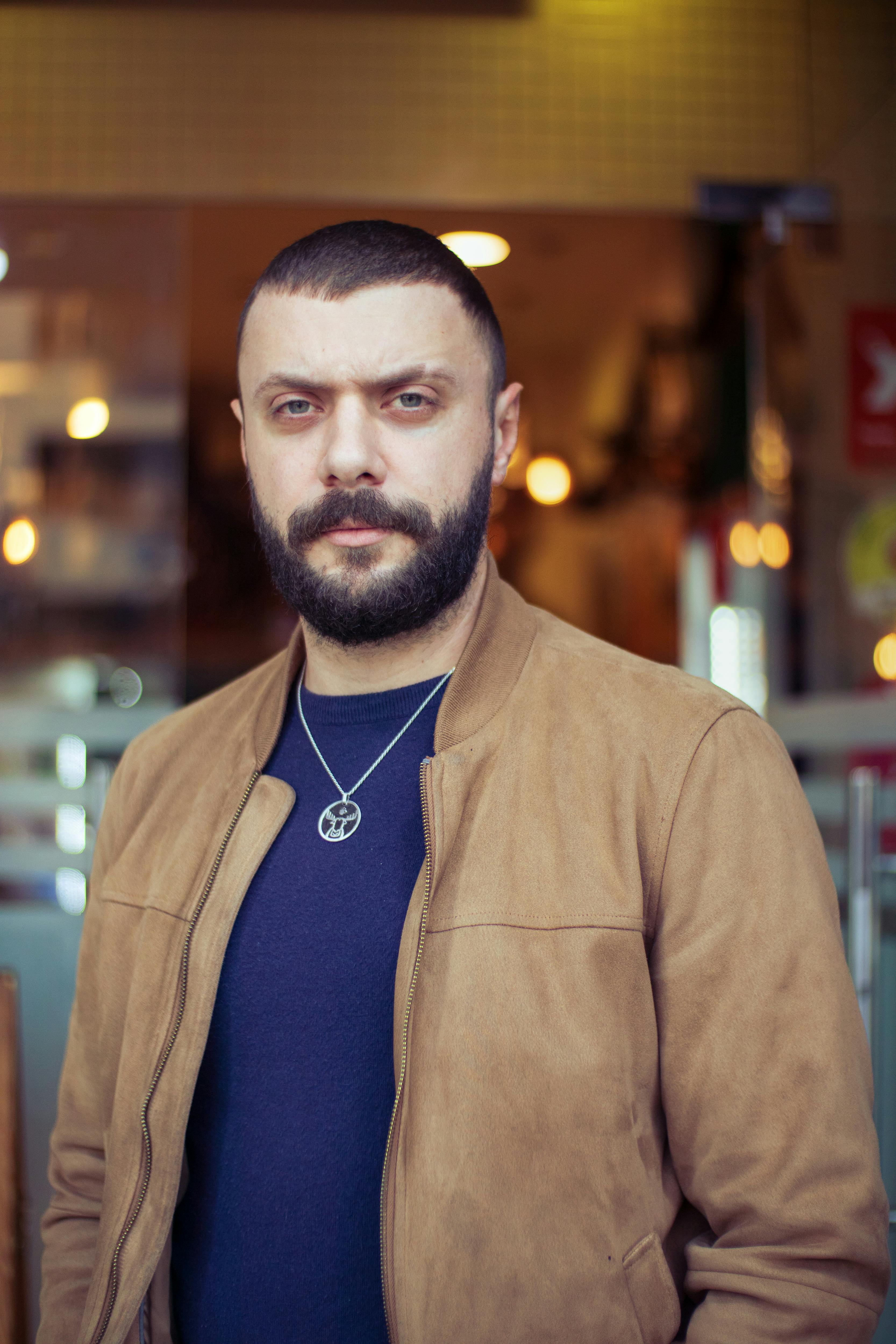 Stylish bearded man wearing a pendant in an urban setting, showcasing modern fashion.