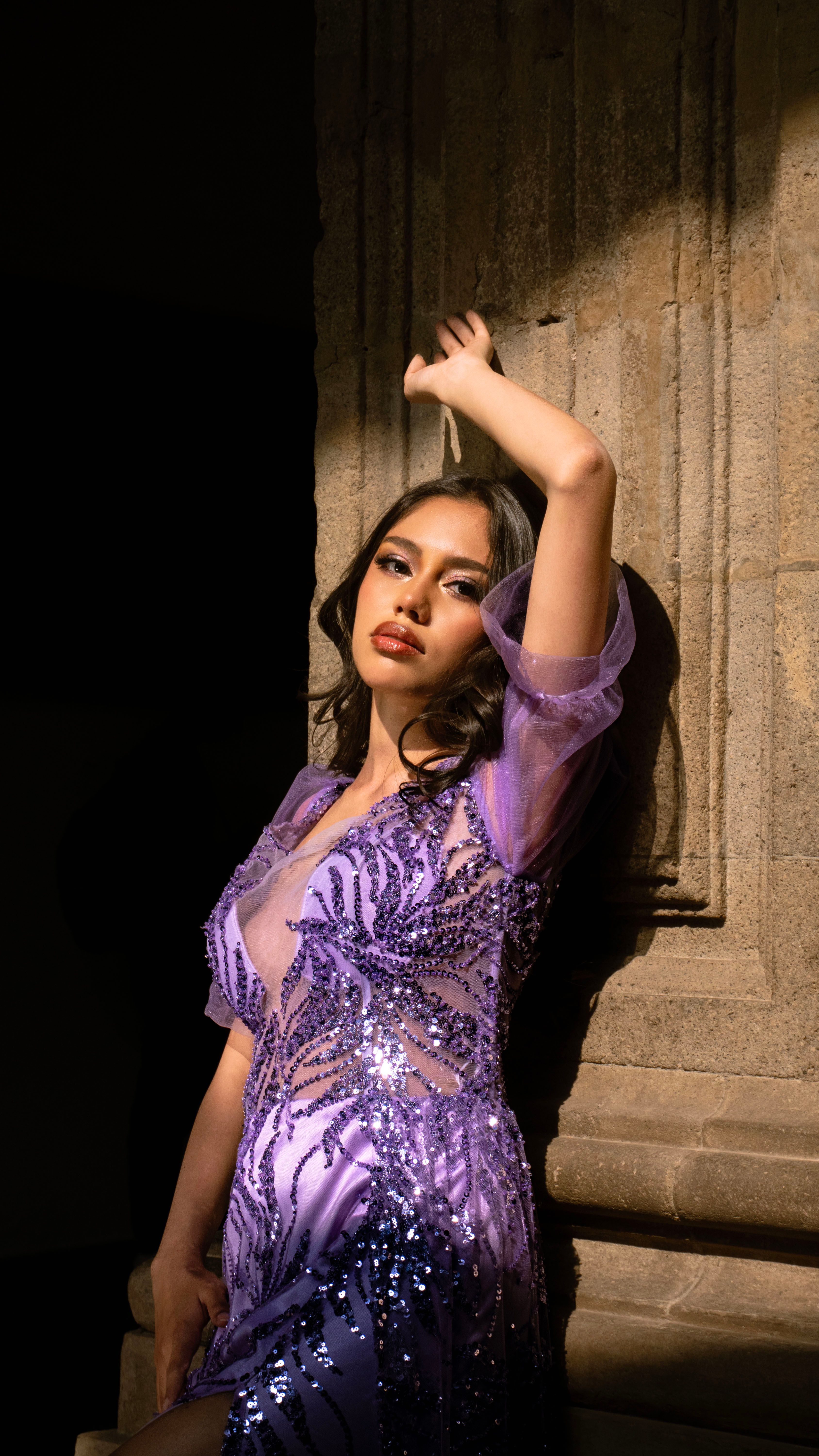 Fashionable woman in a shimmering purple dress posing against vintage architecture.