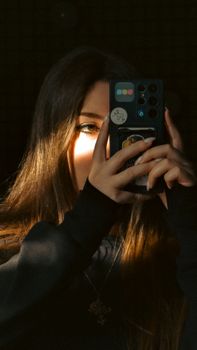 A young woman capturing a selfie with her smartphone, illuminated by warm light, creating a dramatic effect.