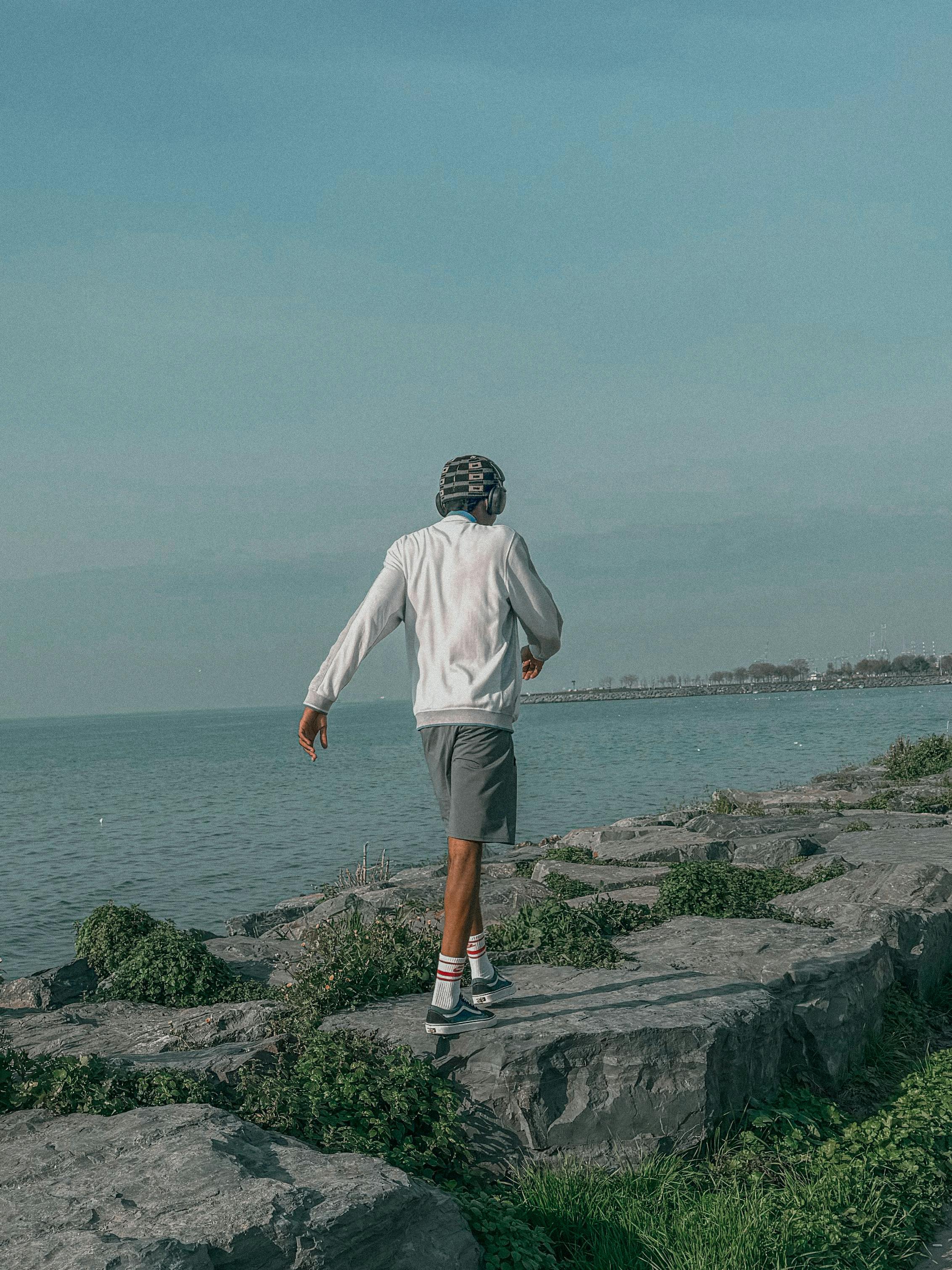 Free Casual man walking along a rocky coastline under a clear blue sky, embracing nature. Stock Photo
