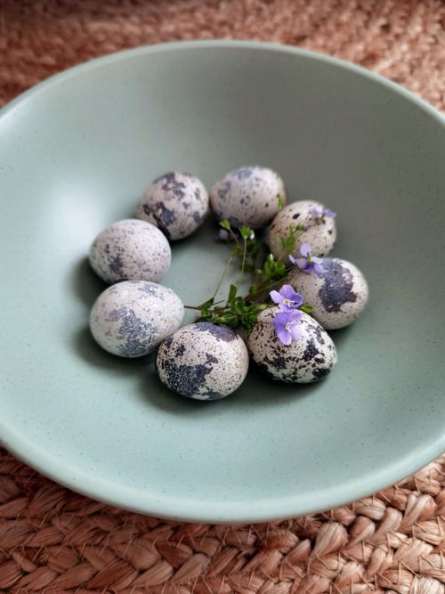 Free Quail eggs and flowers beautifully arranged in a green ceramic bowl on a woven surface. Stock Photo