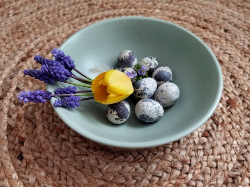 Free A green bowl with quail eggs, yellow tulip, and purple flowers on woven mat. Stock Photo
