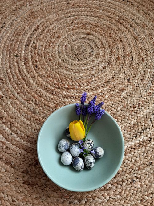 Free Quail eggs with yellow and purple flowers in a pastel bowl on woven texture. Stock Photo