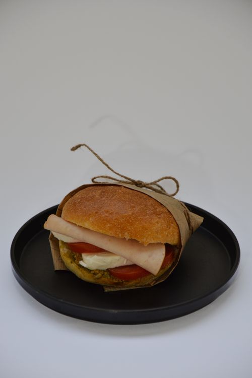 Free Delicious gourmet sandwich with turkey, cheese, and tomato wrapped in paper on a black plate. Stock Photo