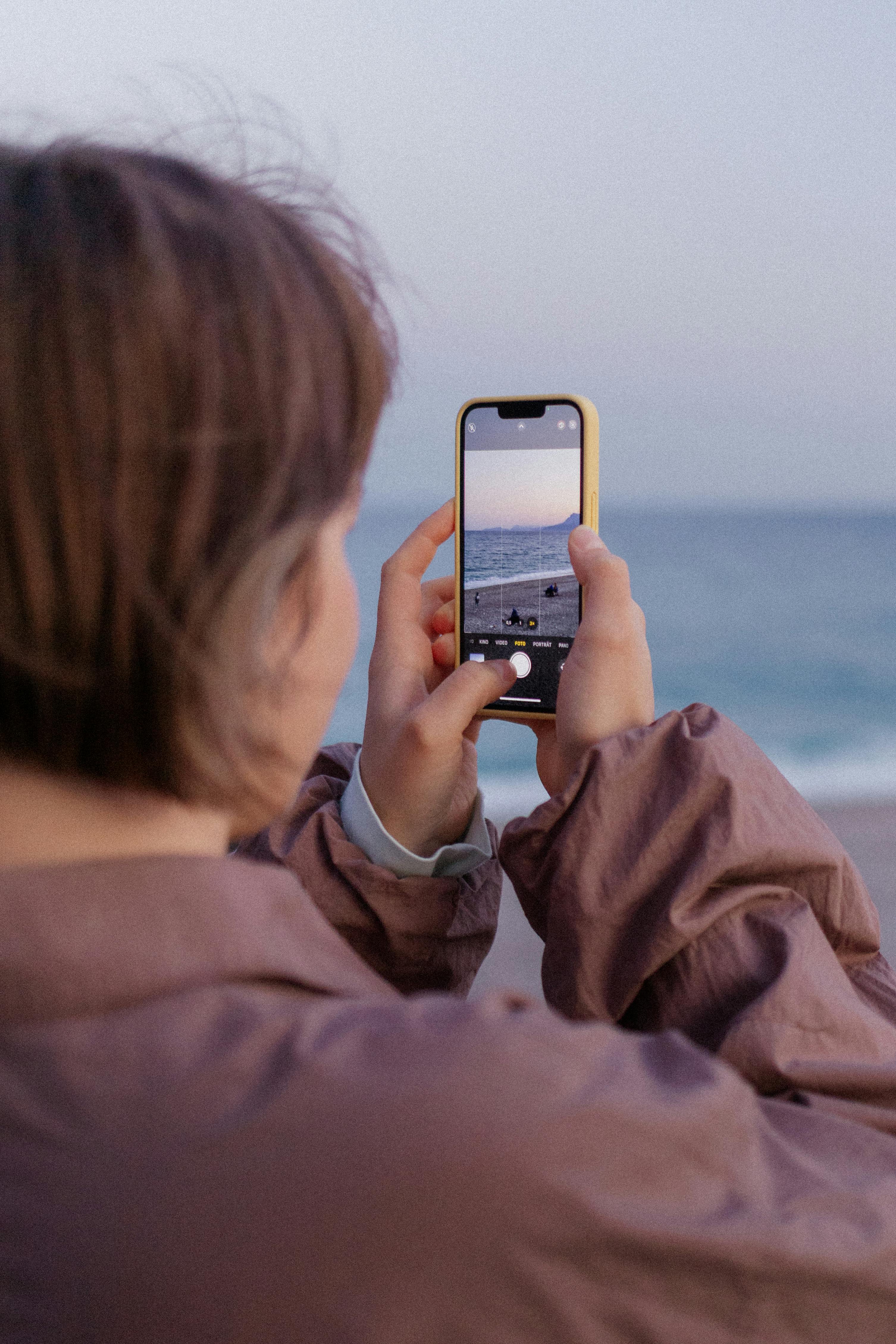 A woman captures a serene ocean view using her smartphone on a summer day.