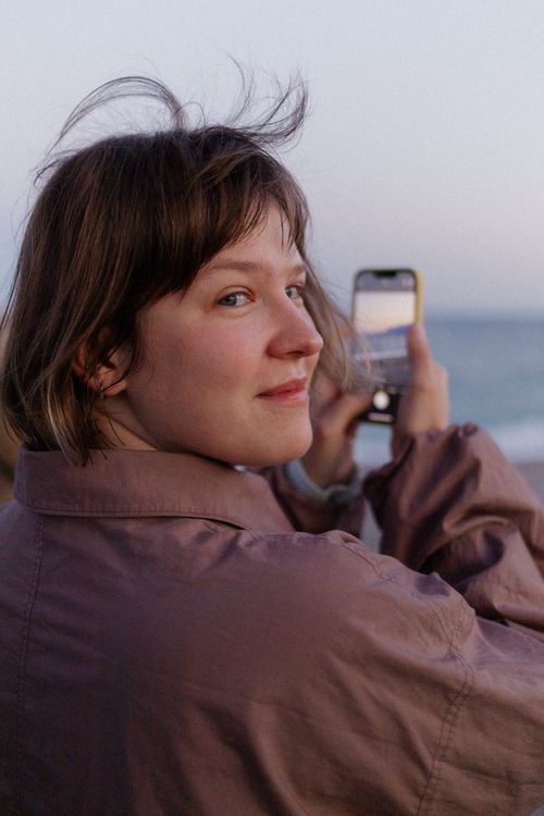 Free Portrait of a smiling woman capturing a beautiful Antalya beach sunset with her smartphone. Stock Photo
