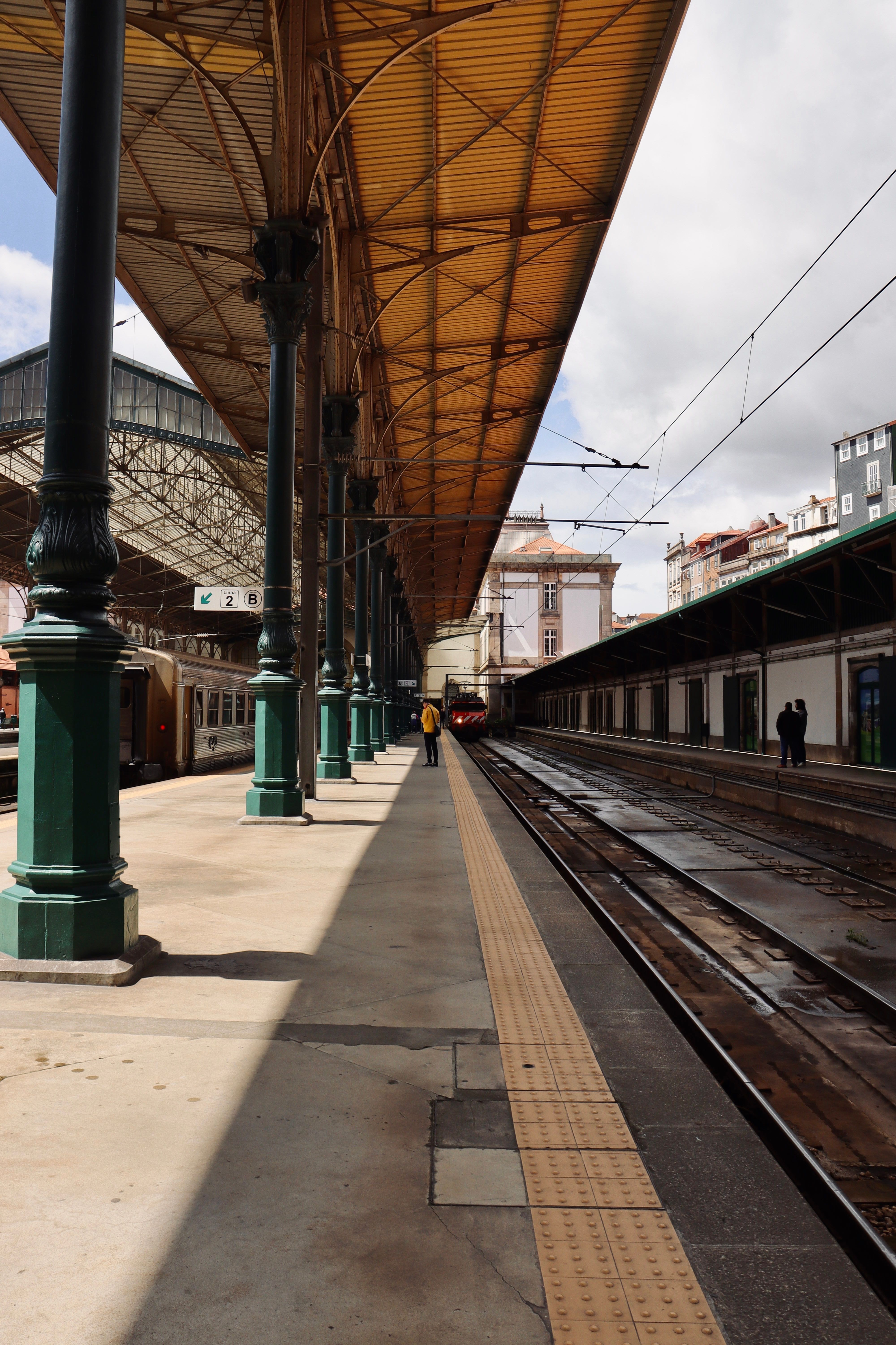 Wide-angle view of a historic train station with iron columns and tracks under a sunny sky. — Estação, Portugal.
