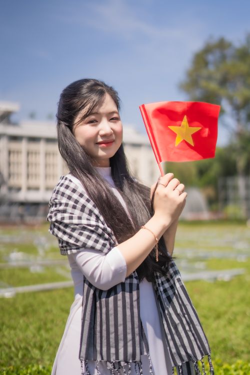 Free Portrait of a young woman outdoors holding the Vietnamese flag on a sunny day. Stock Photo
