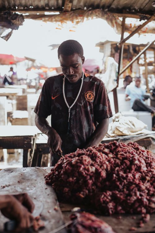 Free A man is focused on preparing meat at a bustling outdoor market stall, showcasing daily life in action. Stock Photo