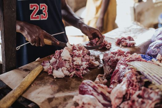 A butcher cutting fresh meat on a market table with a cleaver, showcasing a traditional butchery setting.