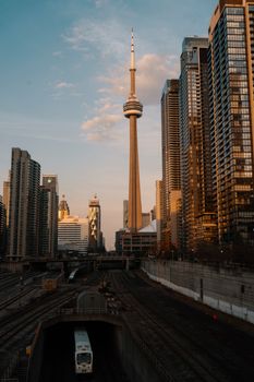 Scenic view of CN Tower and downtown Toronto skyline at sunset, capturing urban architecture and a passing train.