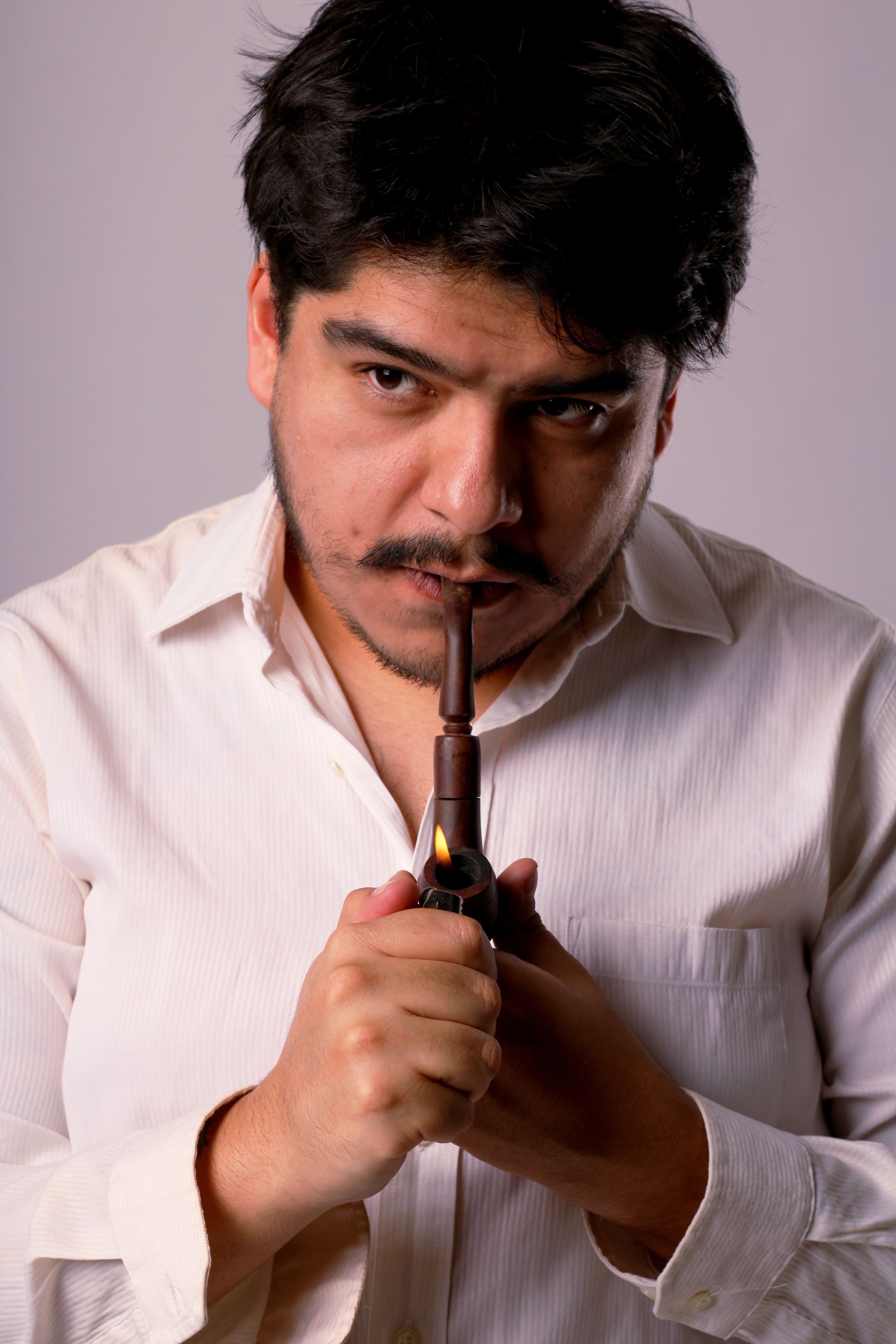 Close-up of a thoughtful man lighting a pipe, wearing a white shirt.