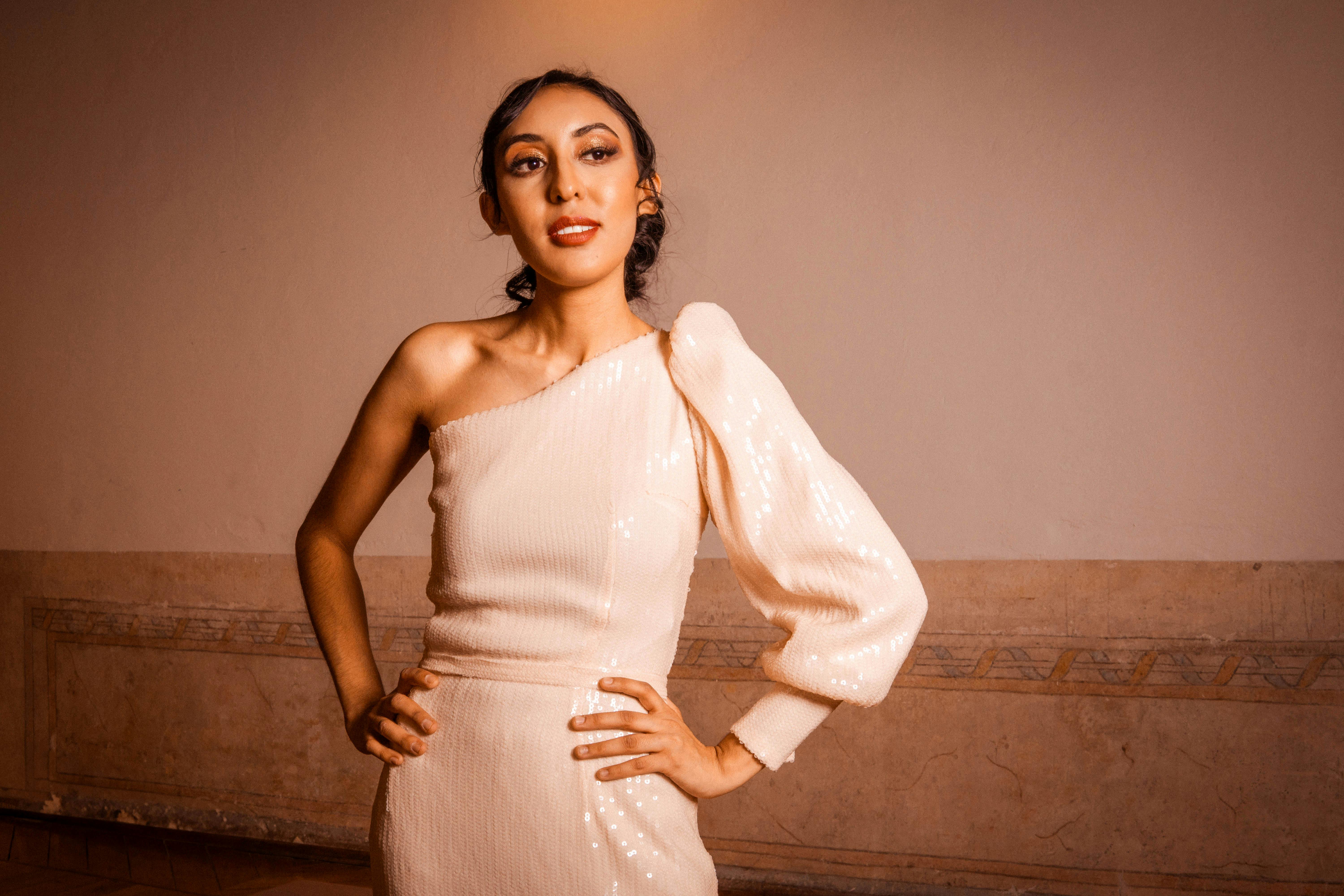 Stylish woman posing indoors in a fashionable one-shoulder dress highlighting elegance.