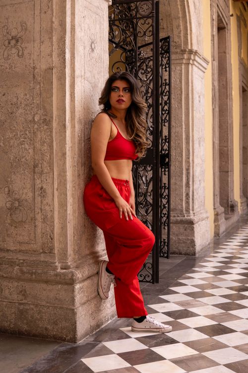 Free Stylish woman in red outfit posing in a classic corridor with checkered floor. Stock Photo