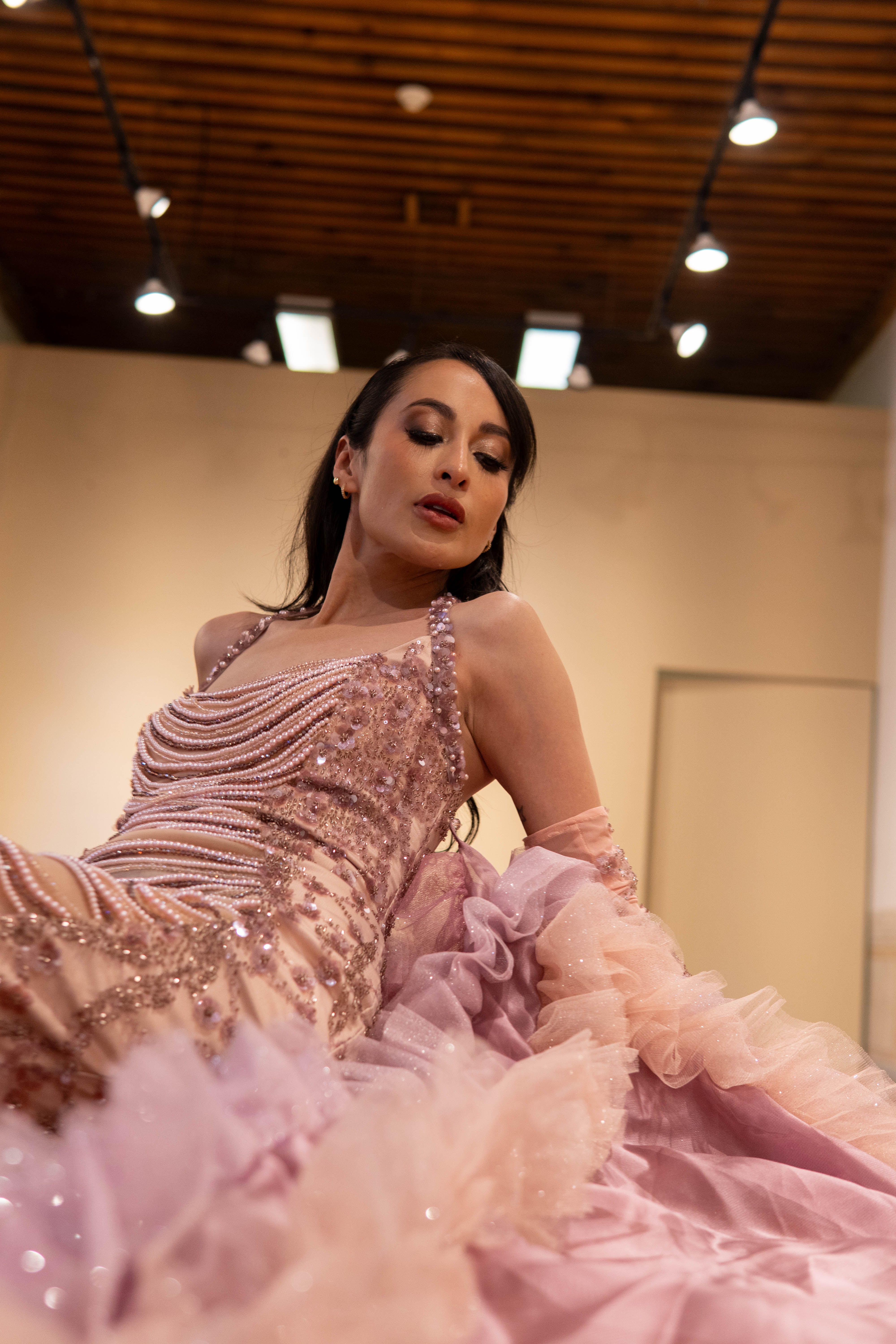 Sophisticated woman posing indoors in a sparkling pink evening gown, capturing elegance and style.