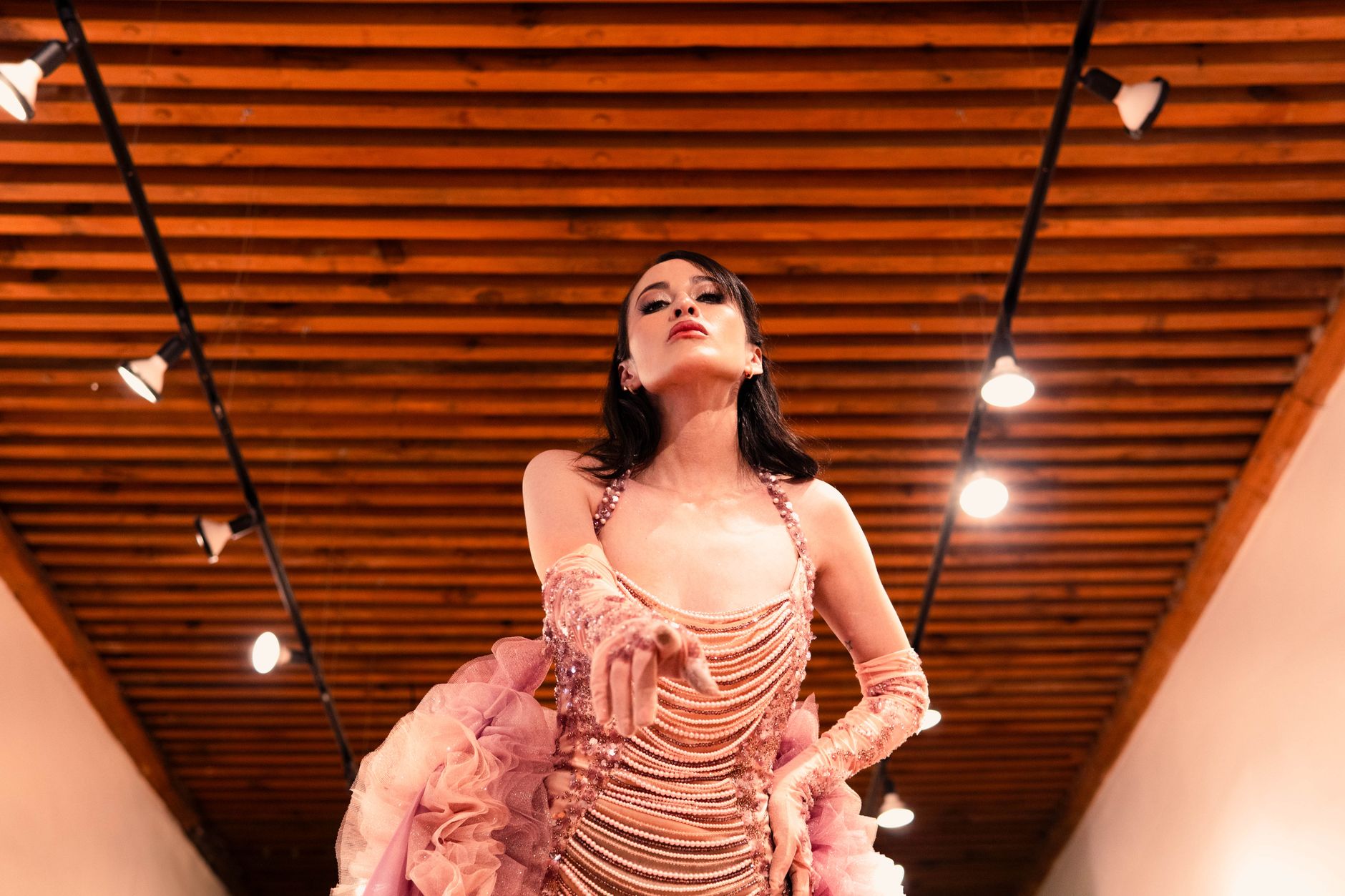 Glamorous fashion model showcasing a detailed pink dress on an indoor runway.