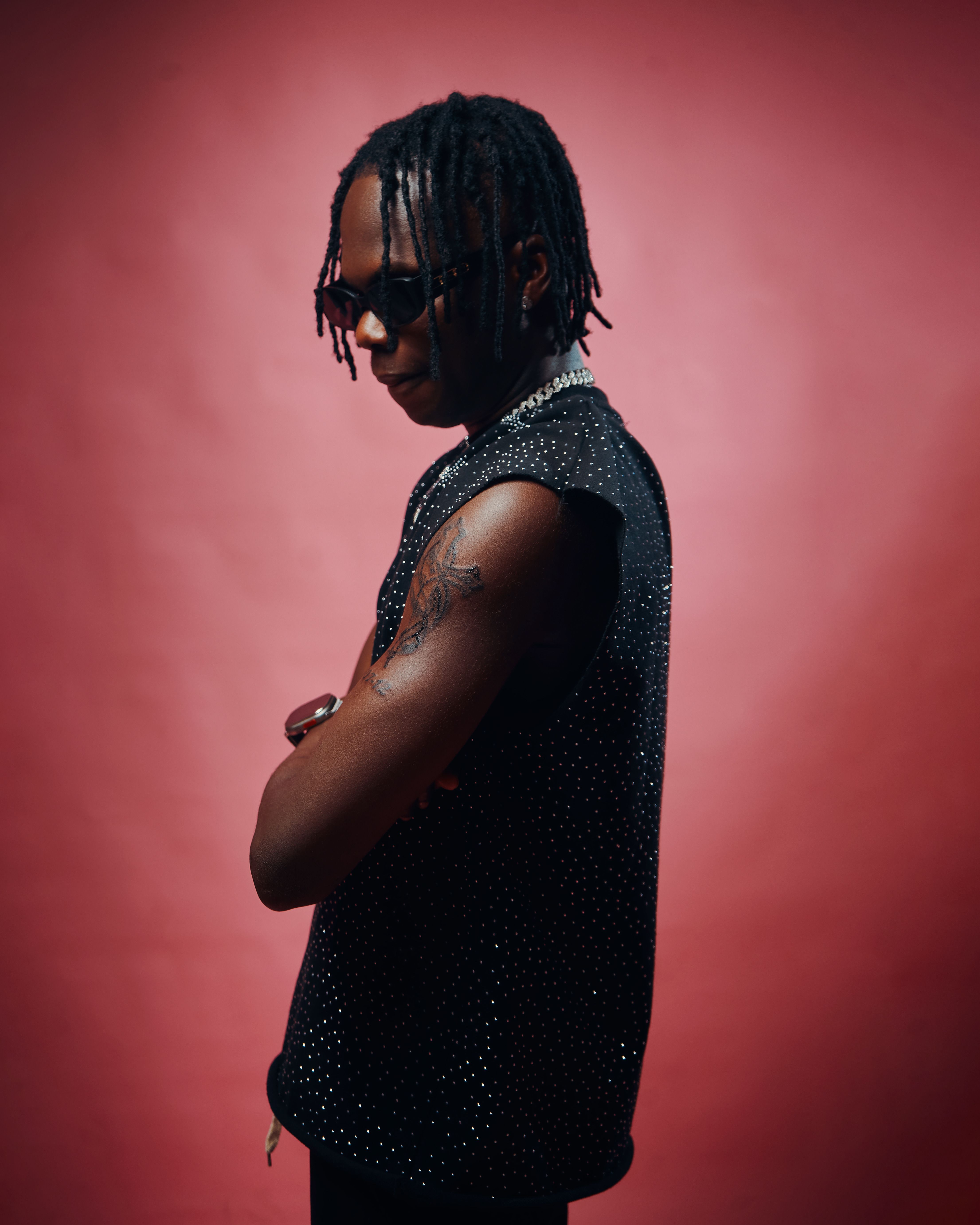 Fashion-forward portrait of an adult in sunglasses standing against a red backdrop.