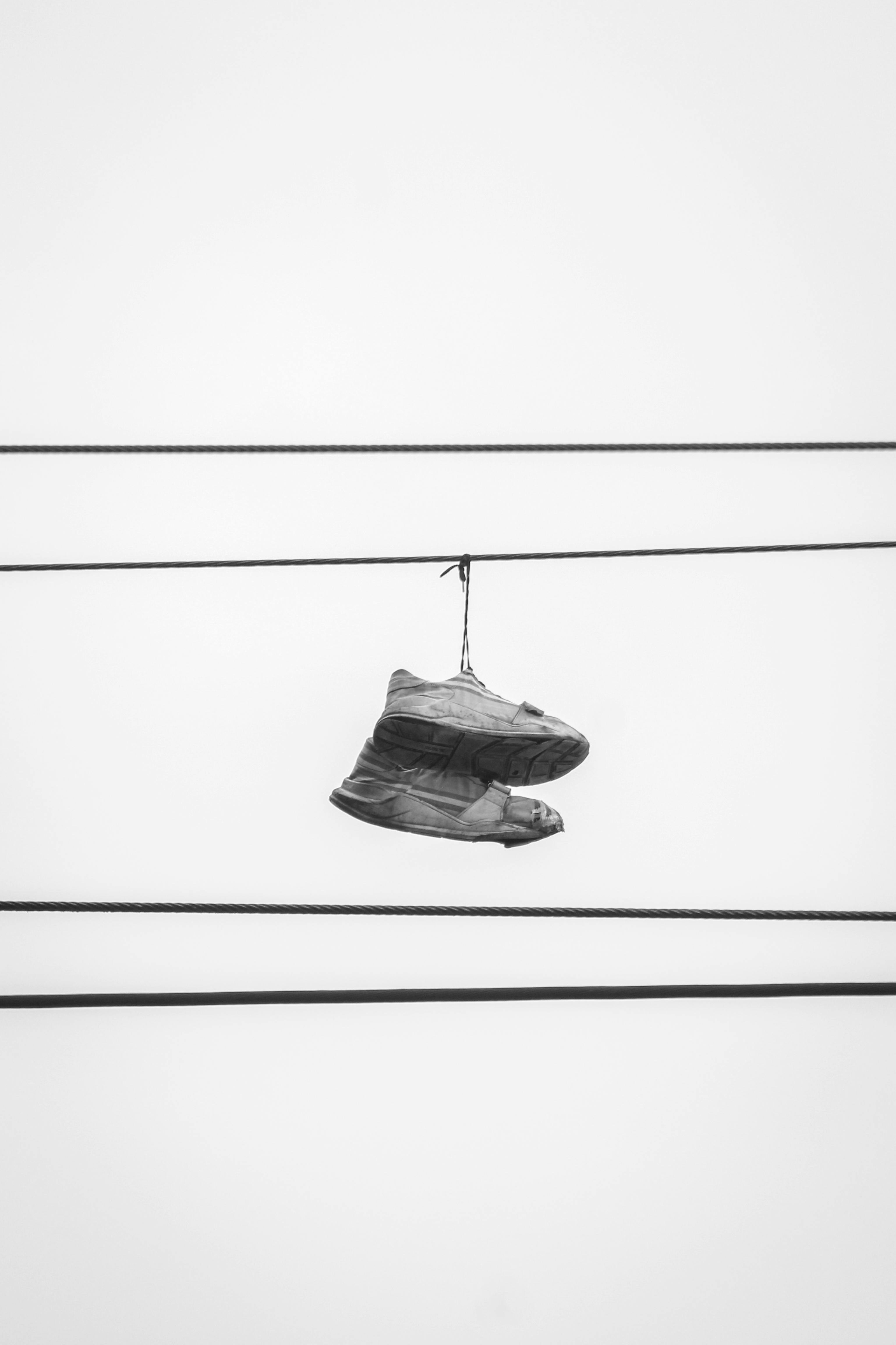 grátis Um par de sapatos pendurados em fios elétricos contra um céu claro. Foto profissional