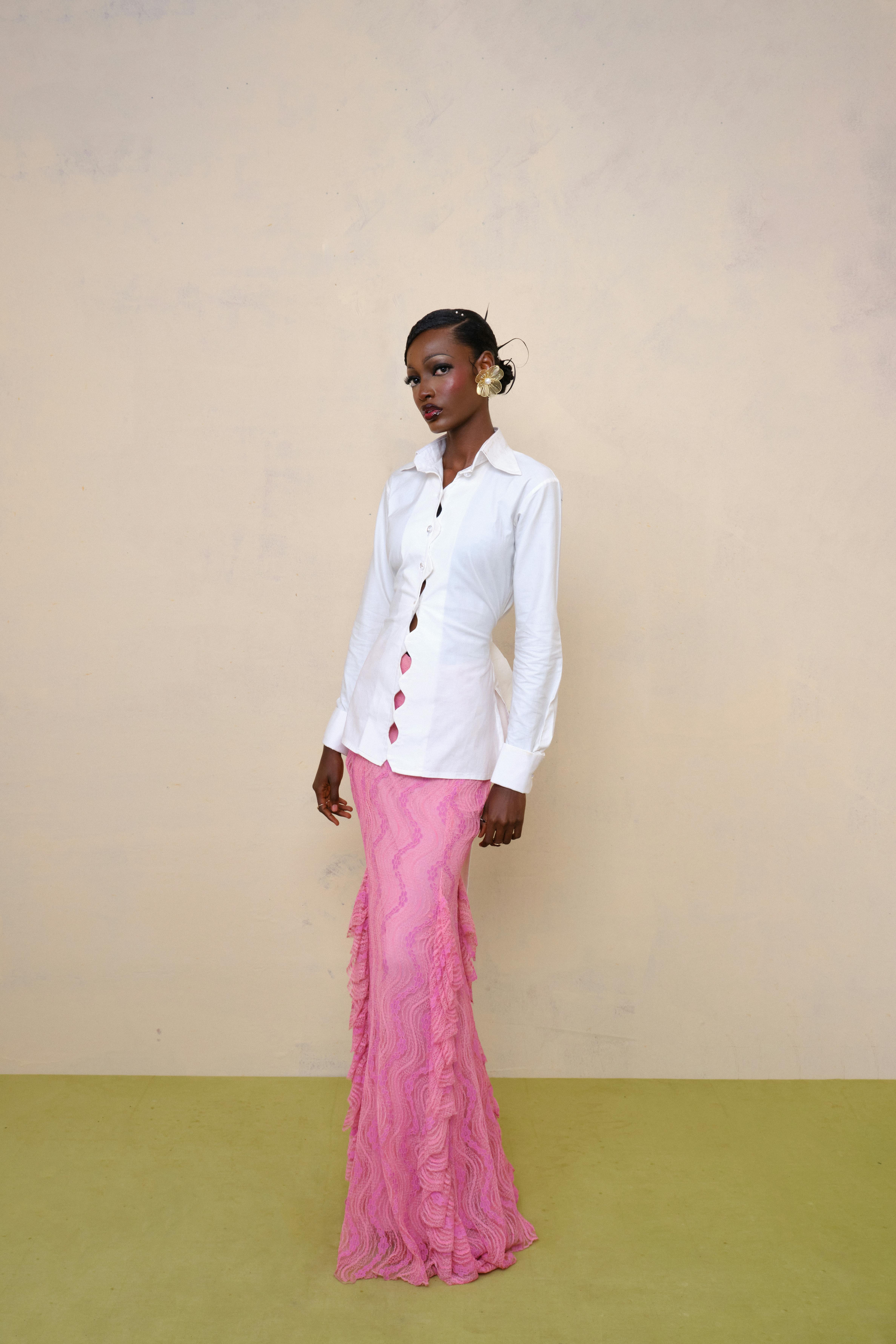 Stylish model poses in a white shirt and pink skirt against a neutral background.