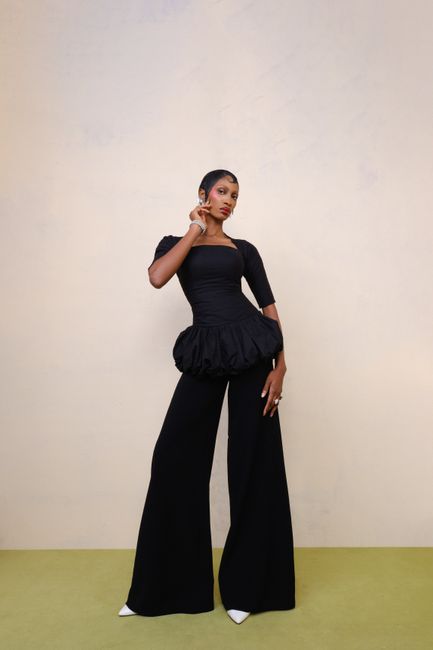 A fashionable model poses elegantly in a black outfit with flared pants, showcasing modern style.