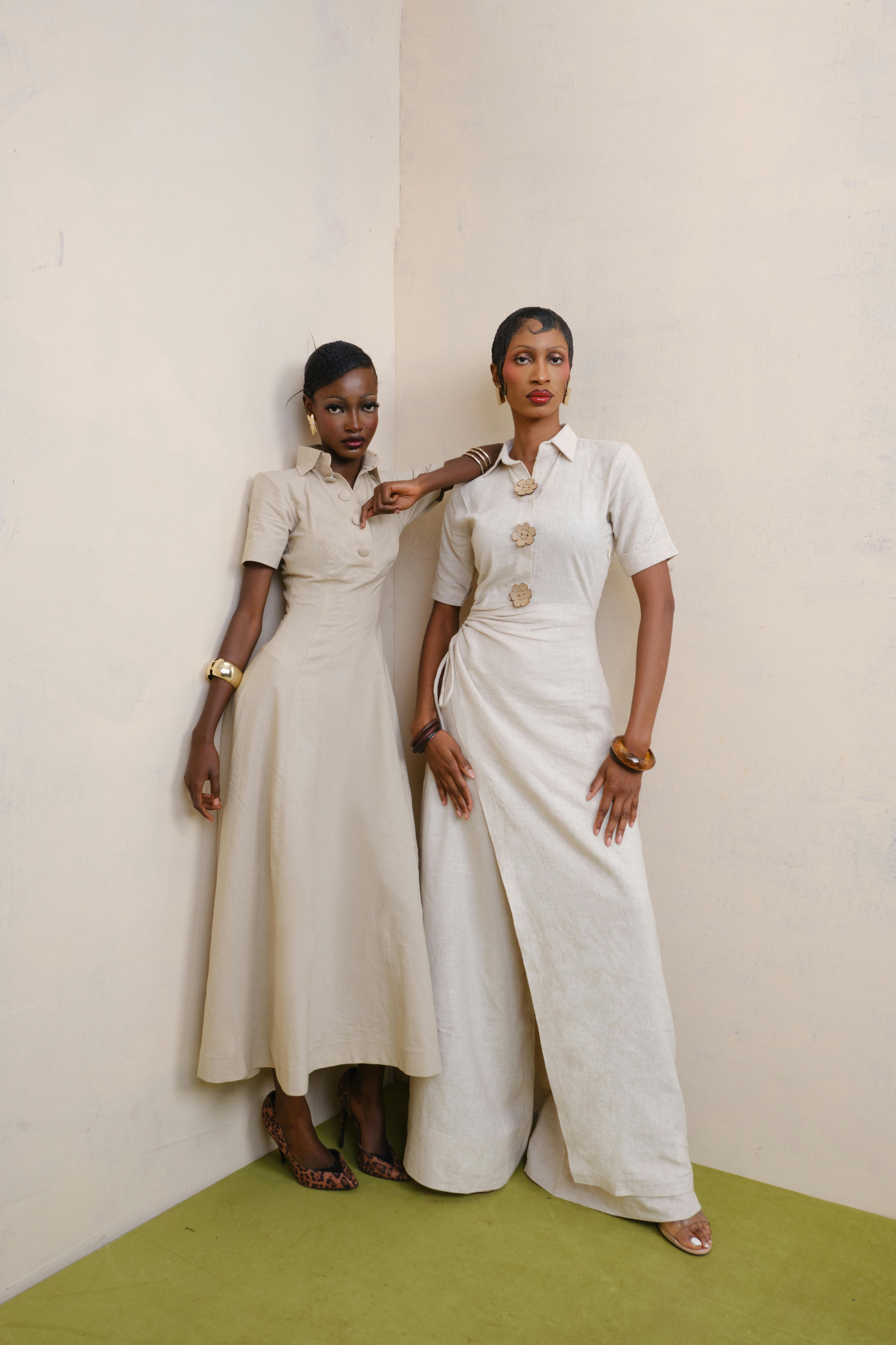 Two stylish women pose in minimalist beige dresses against a neutral background, exuding elegance and fashion.