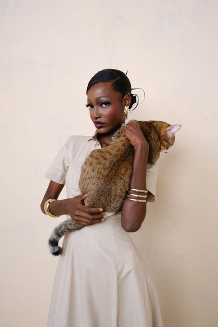 Stylish woman holding a cat in a minimalist setting, exuding poise and elegance.
