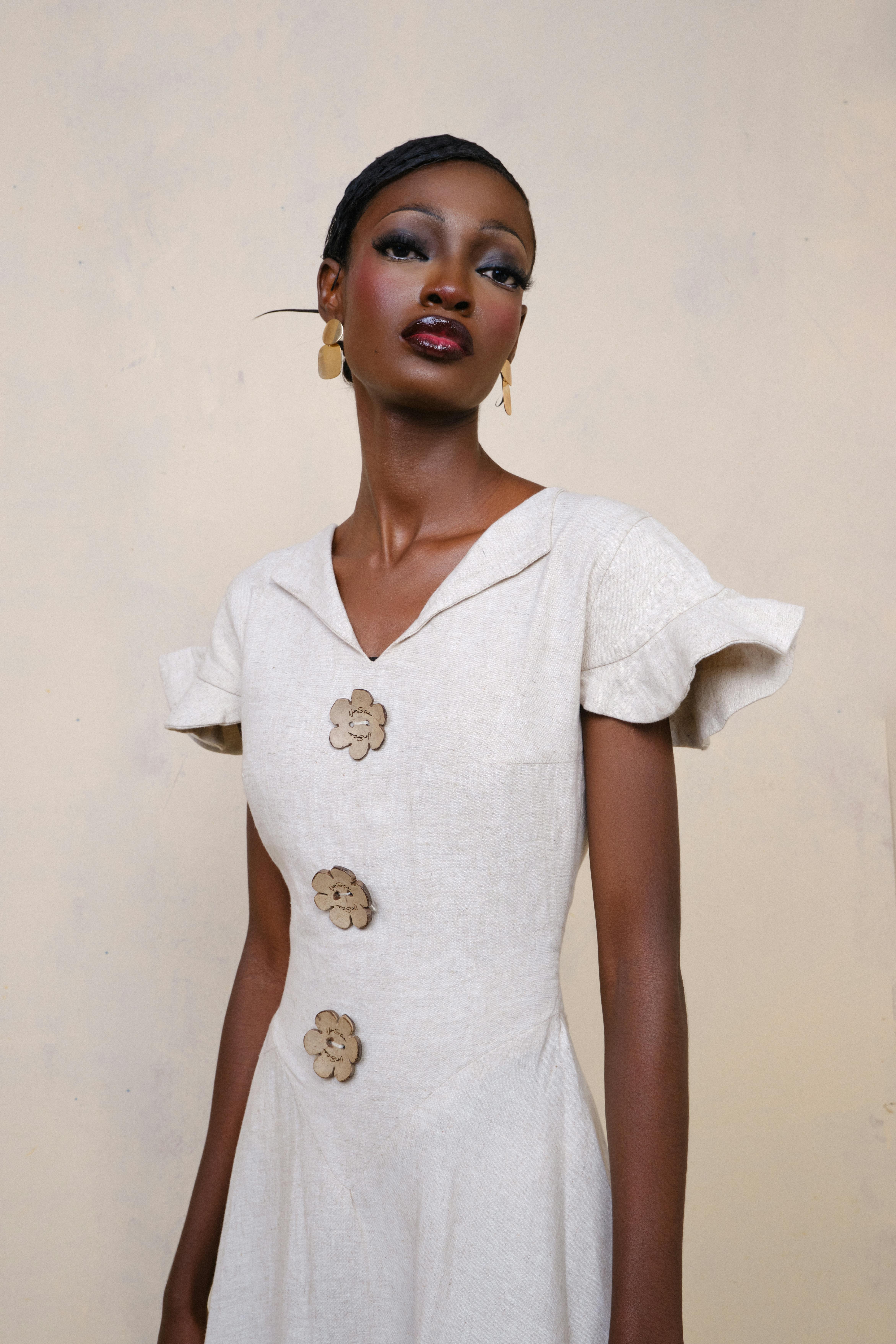 Stylish woman wearing a beige dress with floral buttons, posing gracefully indoors.