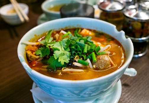A flavorful Thai Tom Yum soup garnished with fresh herbs served in a ceramic bowl.