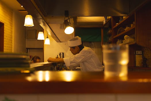 A Japanese chef in uniform focuses on preparing a dish in a cozy Tokyo restaurant kitchen.
