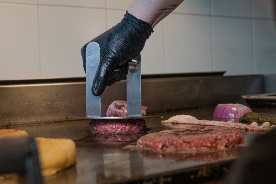 Close-up of a chef cooking a burger on a grill using a metal press, indoors.