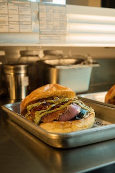 Close-up of a gourmet burger with toppings served on a tray in a restaurant kitchen.