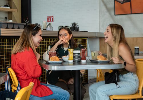 Free Three friends laughing and enjoying burgers in a vibrant city cafe. Stock Photo