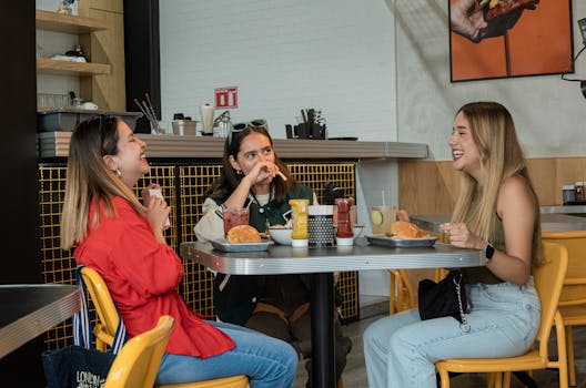 Three friends laughing and enjoying burgers at a modern indoor restaurant setting.