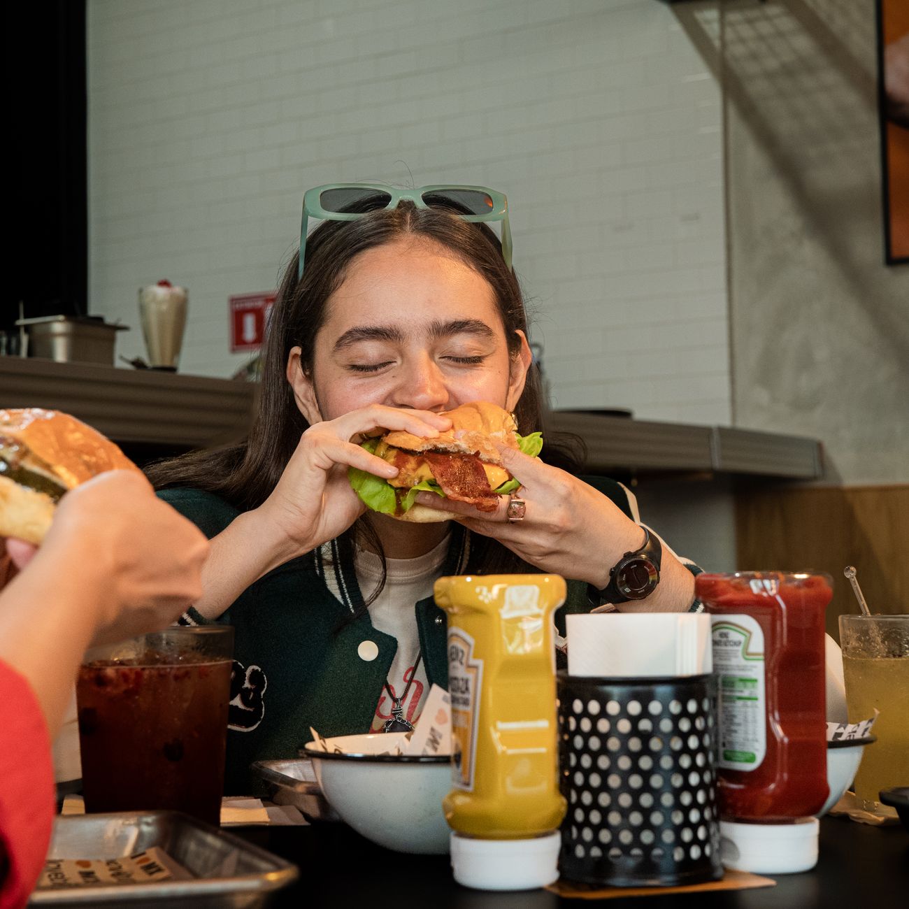 A young woman devours a juicy burger in a casual restaurant setting, surrounded by condiments.