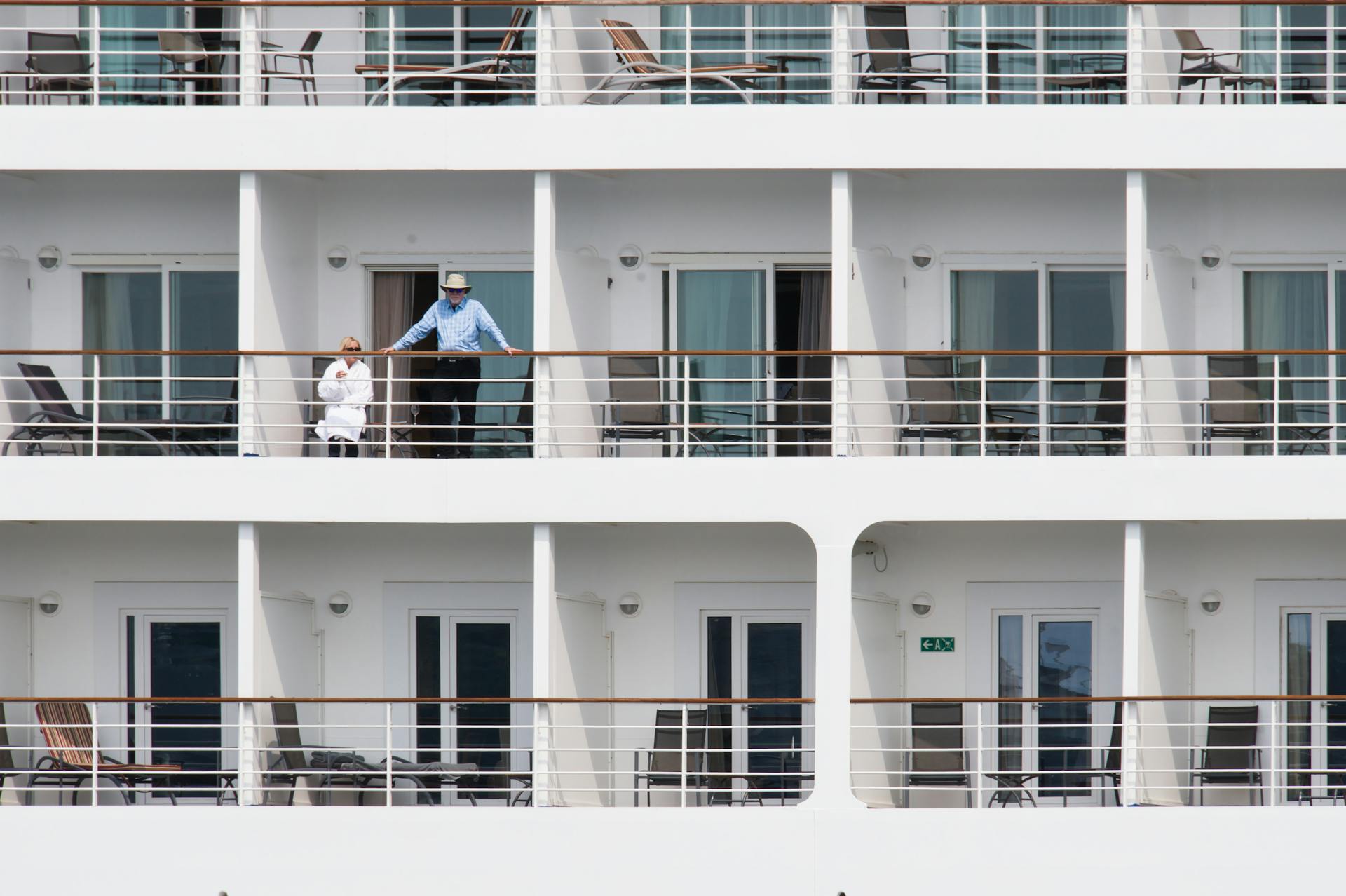A couple enjoys leisure time on a cruise ship balcony, with smooth architecture.