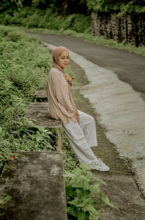 Free Portrait of a young woman wearing a hijab, sitting in a lush outdoor setting in Central Java, Indonesia. Stock Photo
