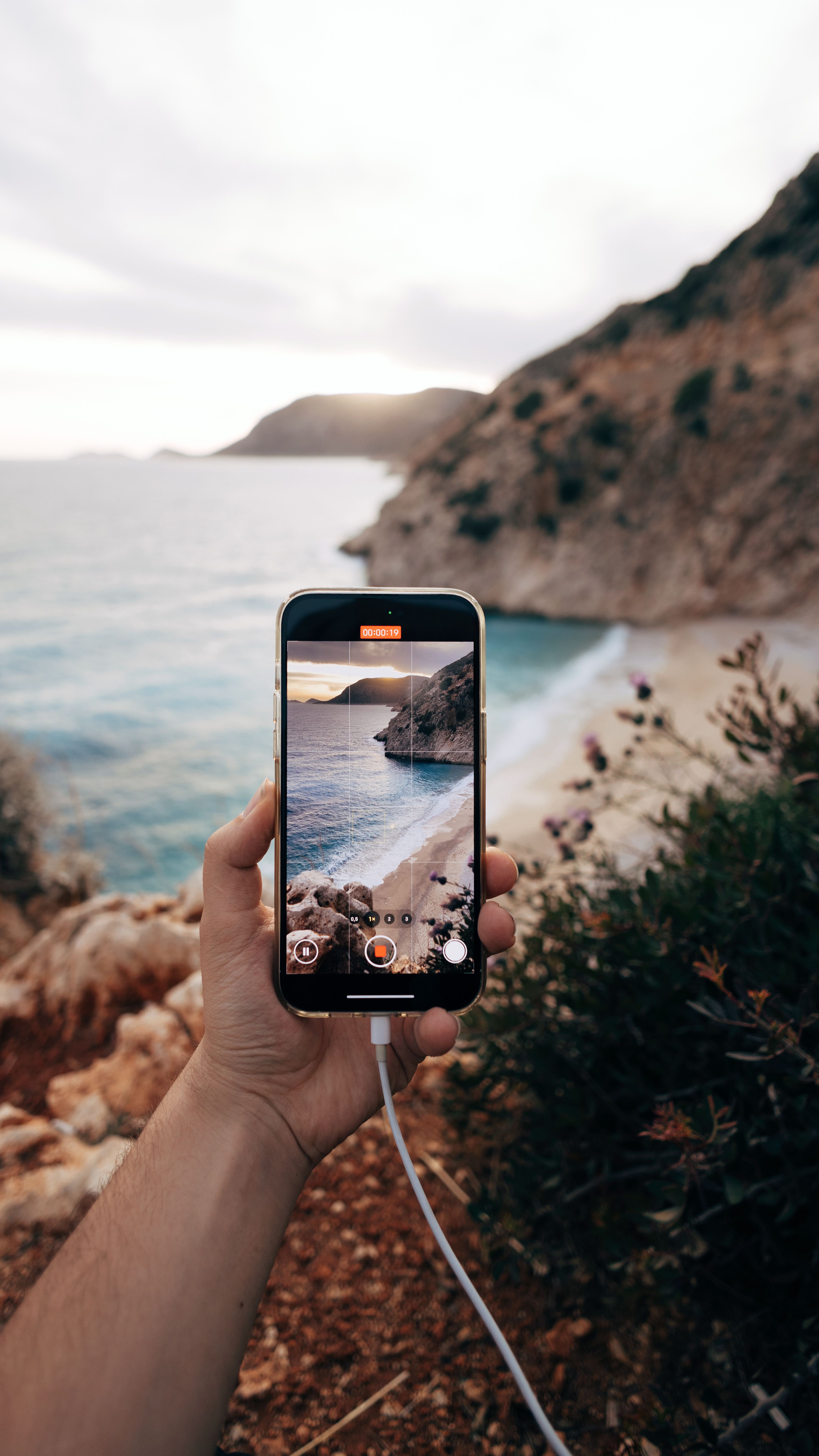 Hand holding smartphone capturing stunning coastal landscape view.