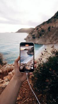 Hand holding smartphone capturing stunning coastal landscape view.