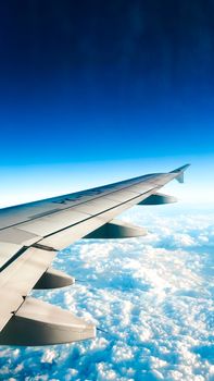 Airplane wing flying above fluffy clouds with a striking blue sky contrast.