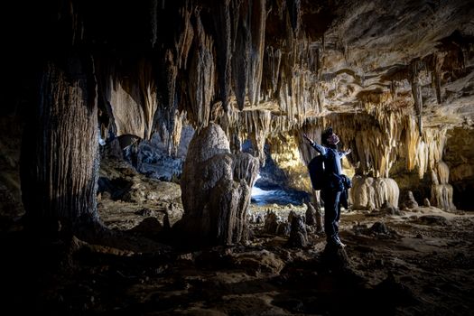 A man admires fascinating stalactites and stalagmites inside a vast cave, illuminated by subtle light.