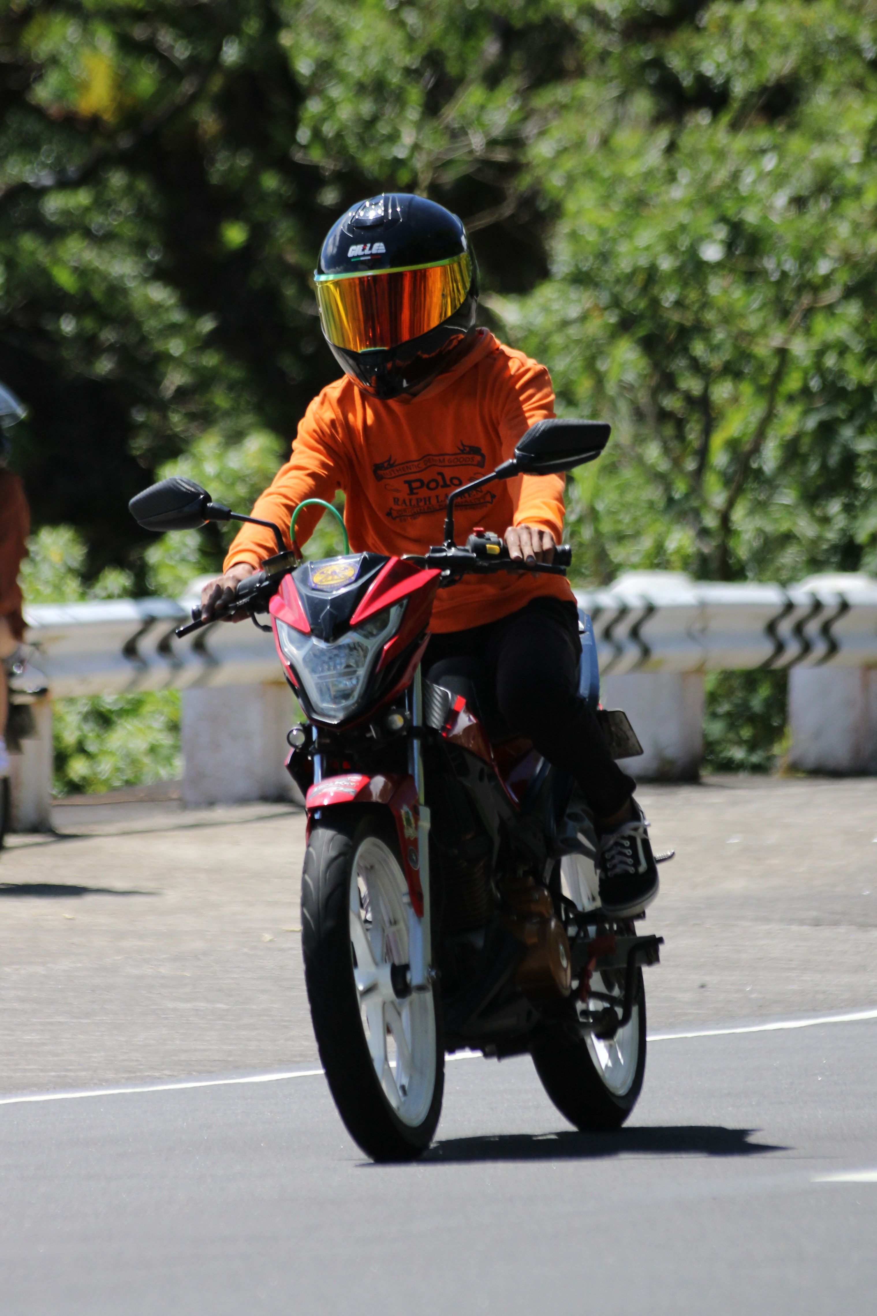 Person riding a motorcycle on a curvy road under bright sunshine.