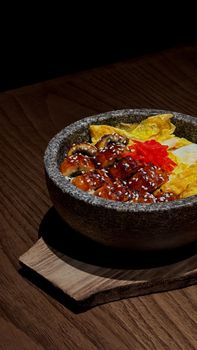 Mouthwatering unagi rice bowl with vibrant toppings in a rustic stone bowl, perfect for Asian cuisine enthusiasts.